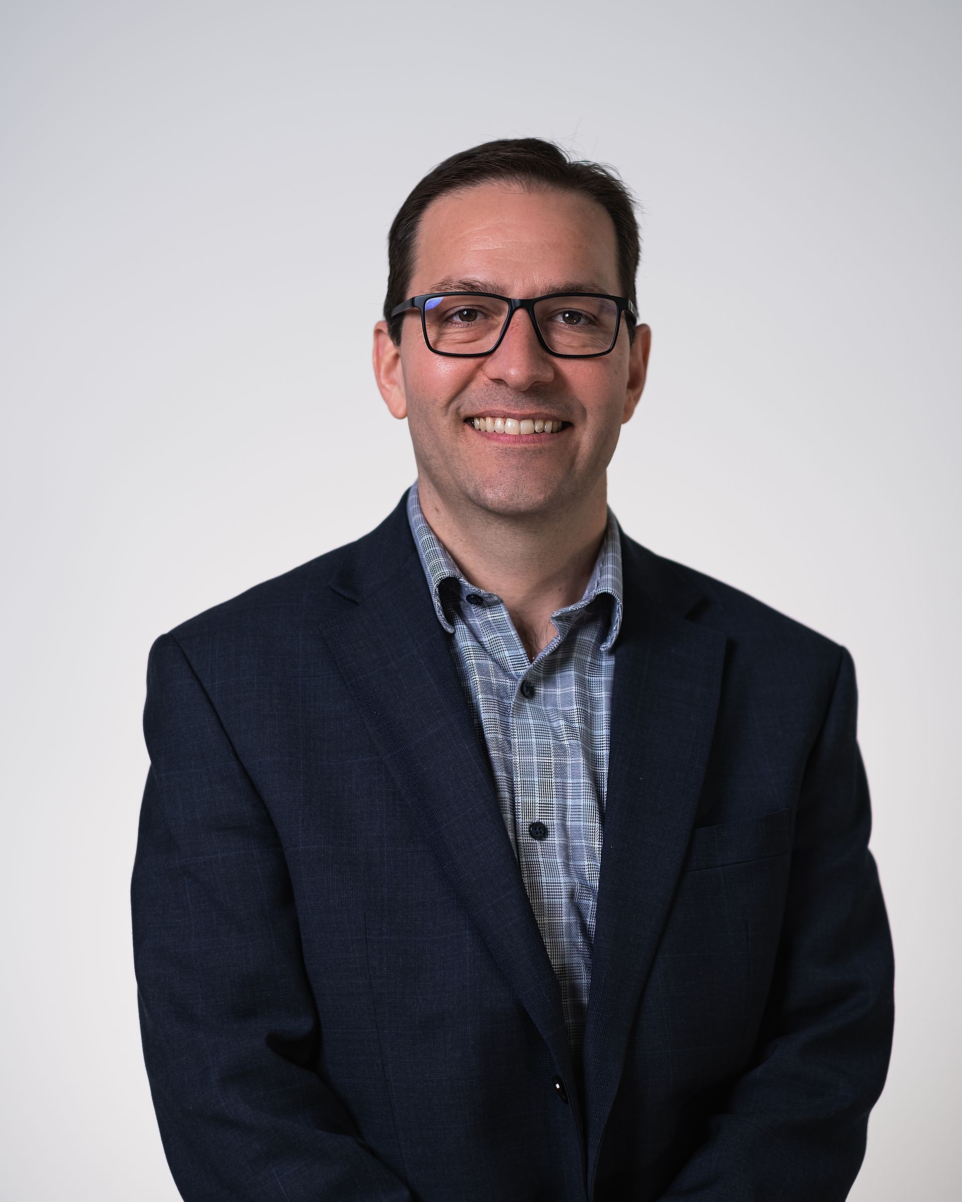 A man wearing glasses and a suit is smiling for the camera.