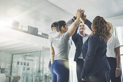 A multicultural team high-fives in an office.