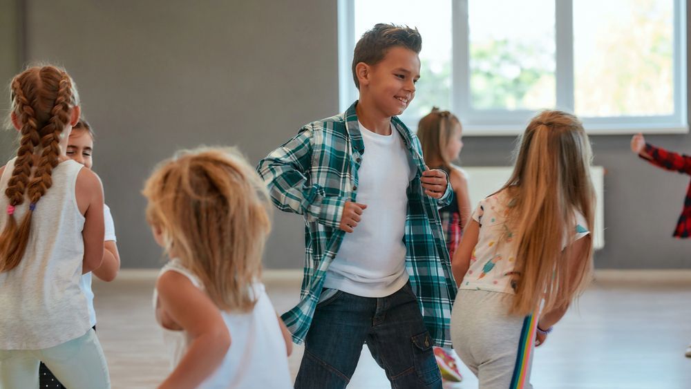 Bambini che ballano in una sala di danza ben illuminata, sorridenti e in movimento.