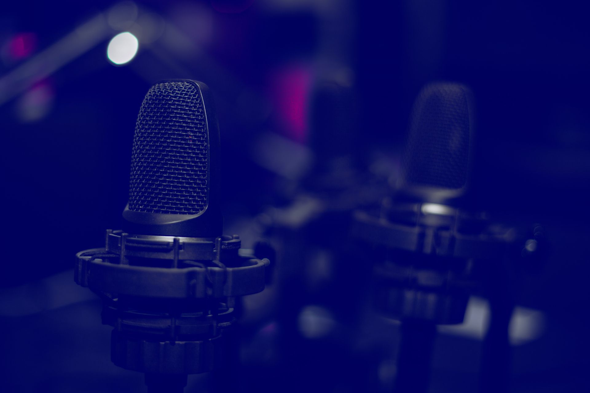 Due microfoni neri su supporti, su uno sfondo blu scuro sfocato con accenni di luce bianca e rosa.