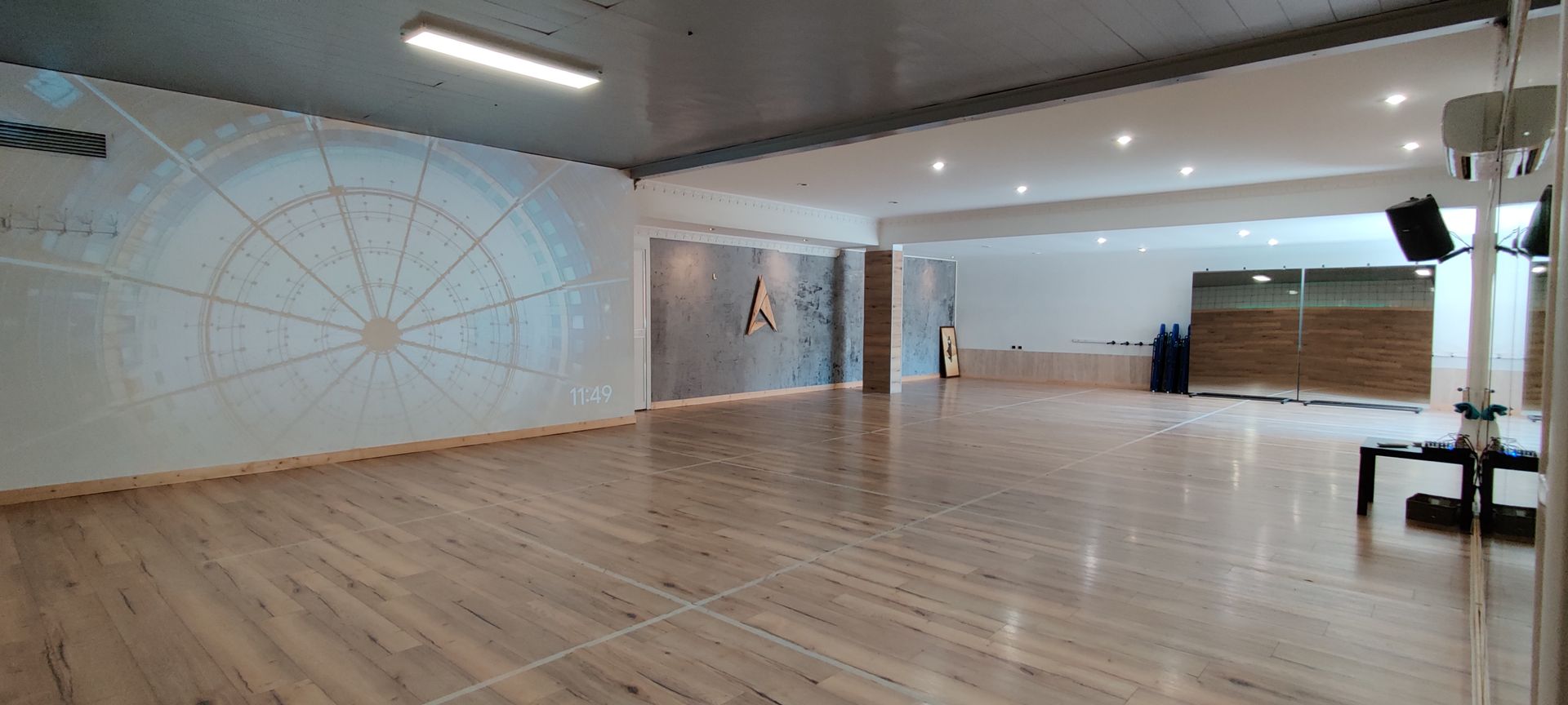 Studio vuoto con pavimento in legno, pareti bianche e un grande disegno circolare sulla parete.