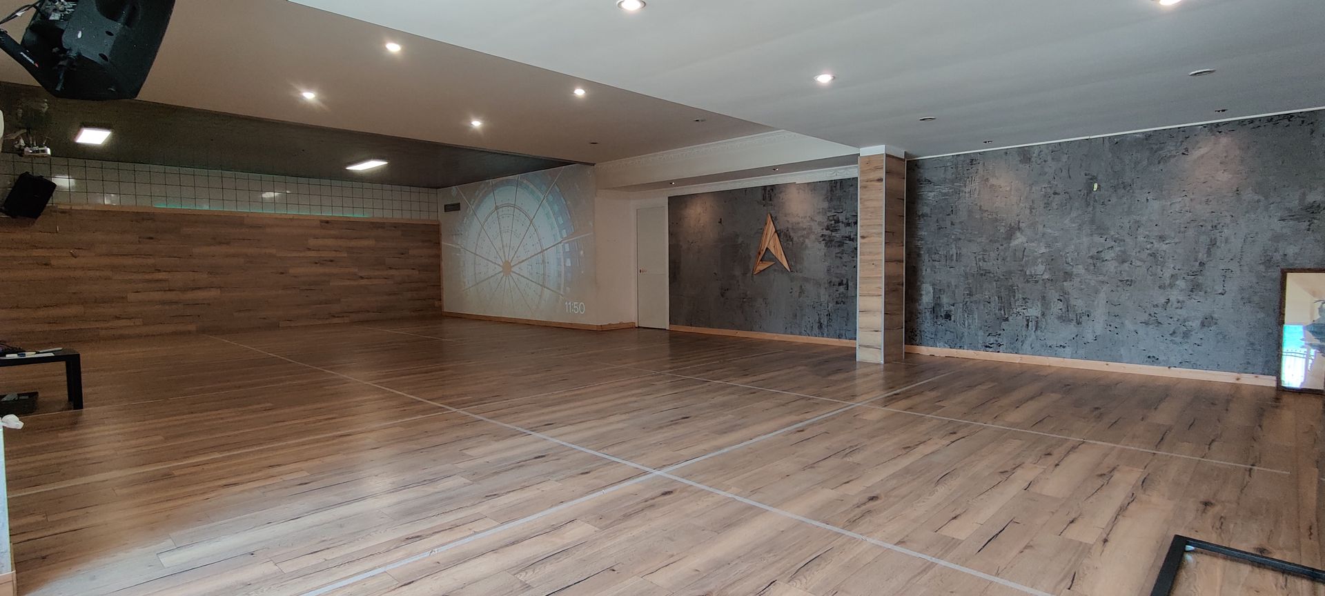 Studio di danza vuoto con pavimento in legno e pareti con texture, colori neutri.