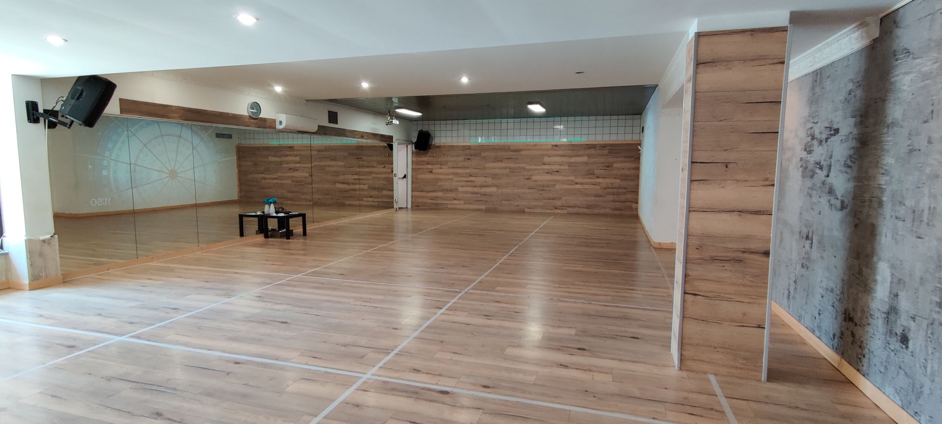 Uno studio di danza spazioso con pavimento e pareti in legno. Uno specchio e degli altoparlanti sono appesi alle pareti.