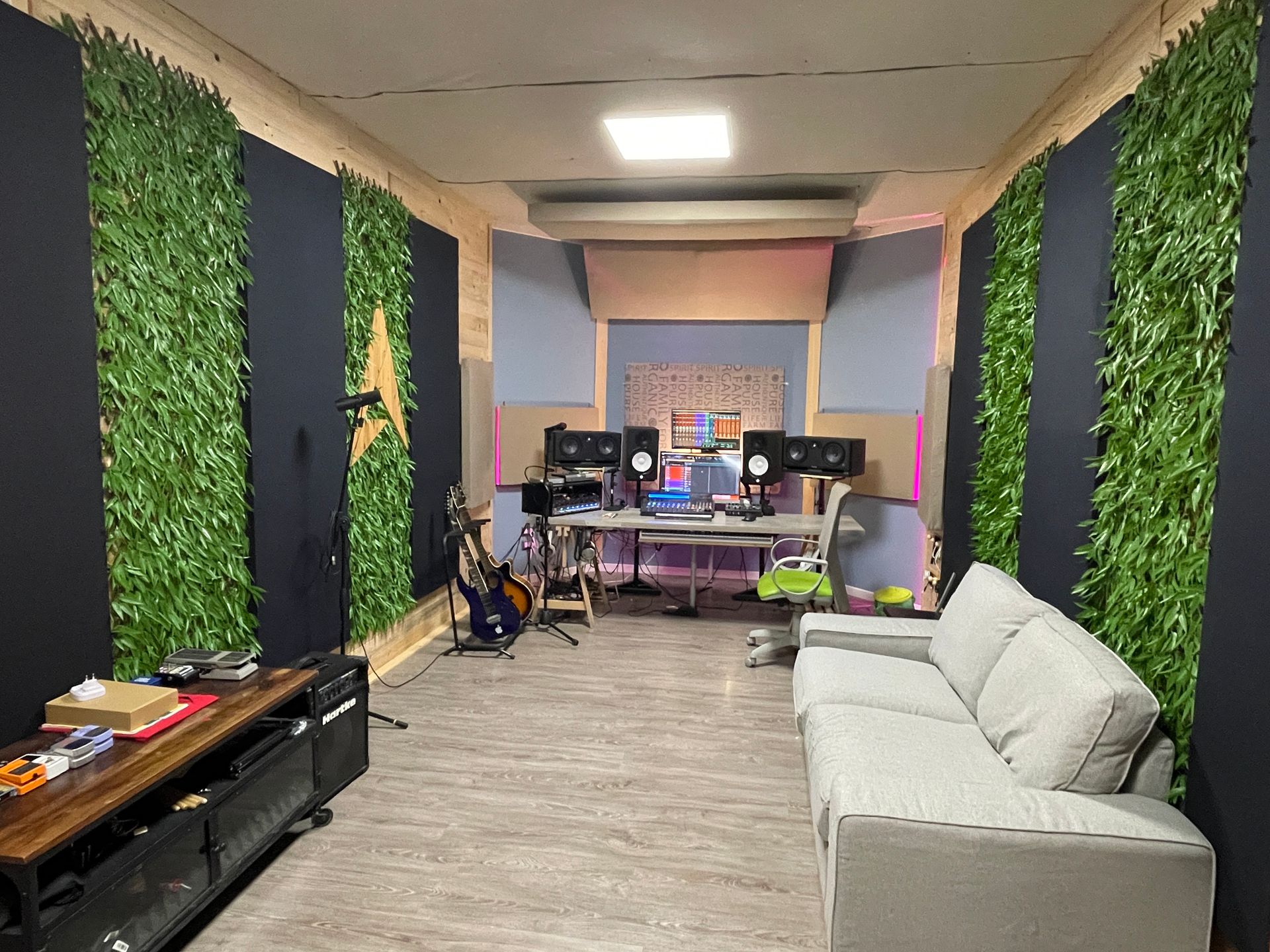 Studio di registrazione: pareti verdi, divano grigio, strumenti, computer, toni neutri.