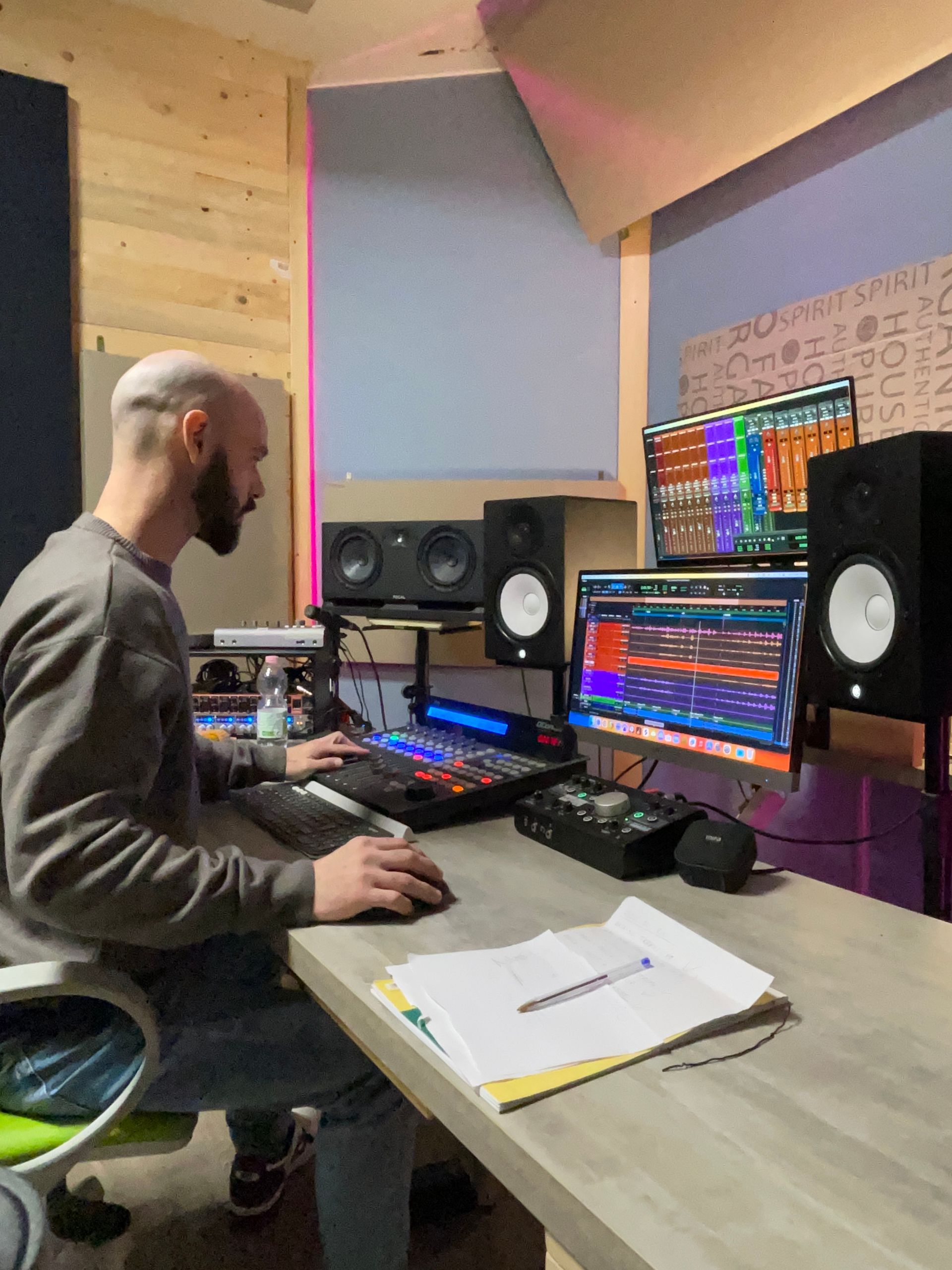 Uomo al computer in uno studio musicale, che modifica l'audio con monitor, altoparlanti e console di missaggio.