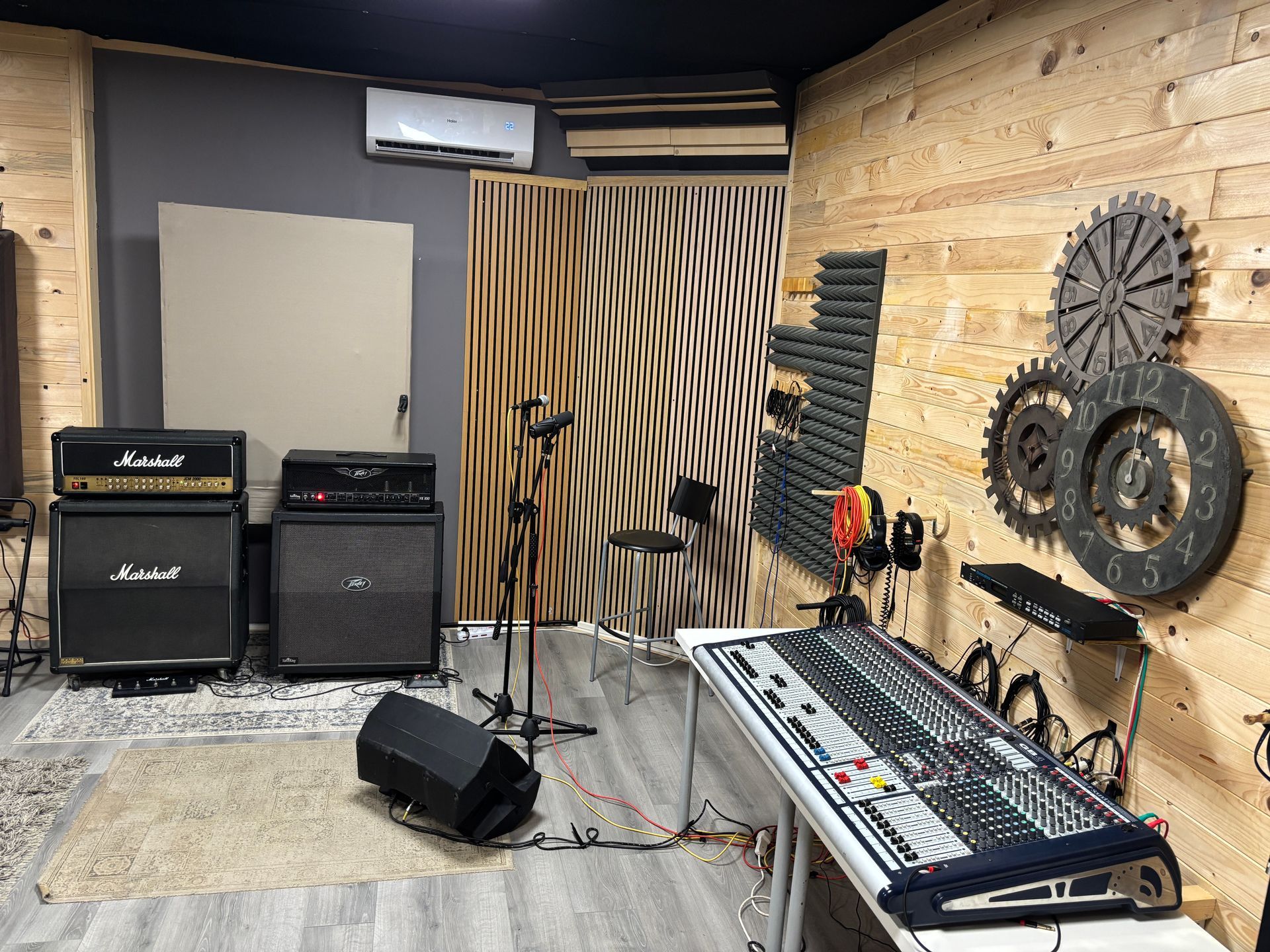 Studio di registrazione con amplificatori Marshall, console di missaggio, microfoni e insonorizzazione, con dettagli in legno e grigio.