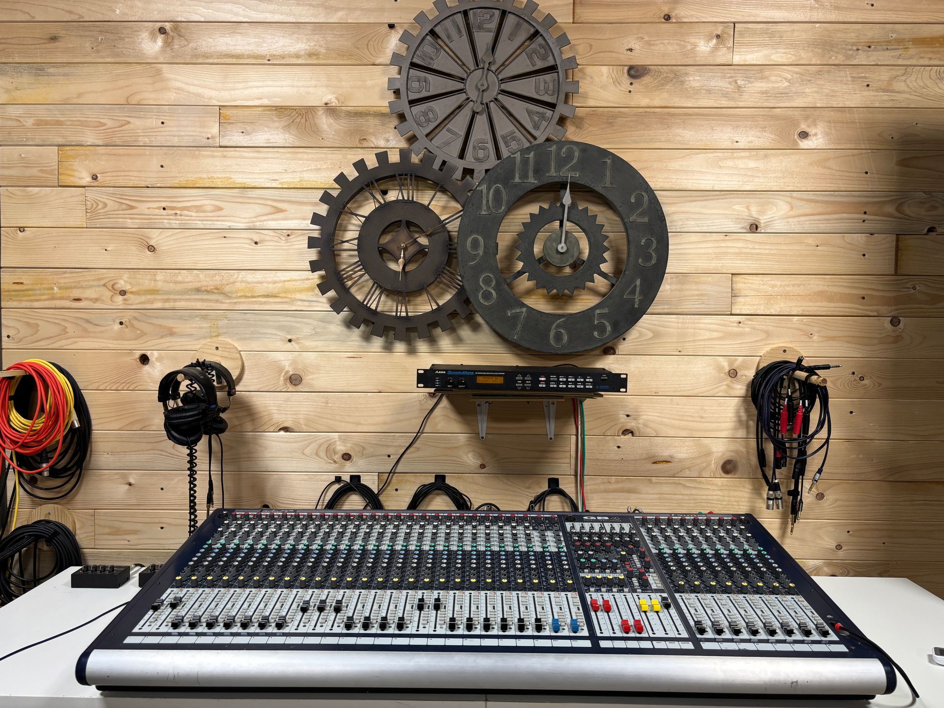 Console di mixaggio audio su un tavolo bianco, con decorazioni murali a forma di ingranaggio dietro.