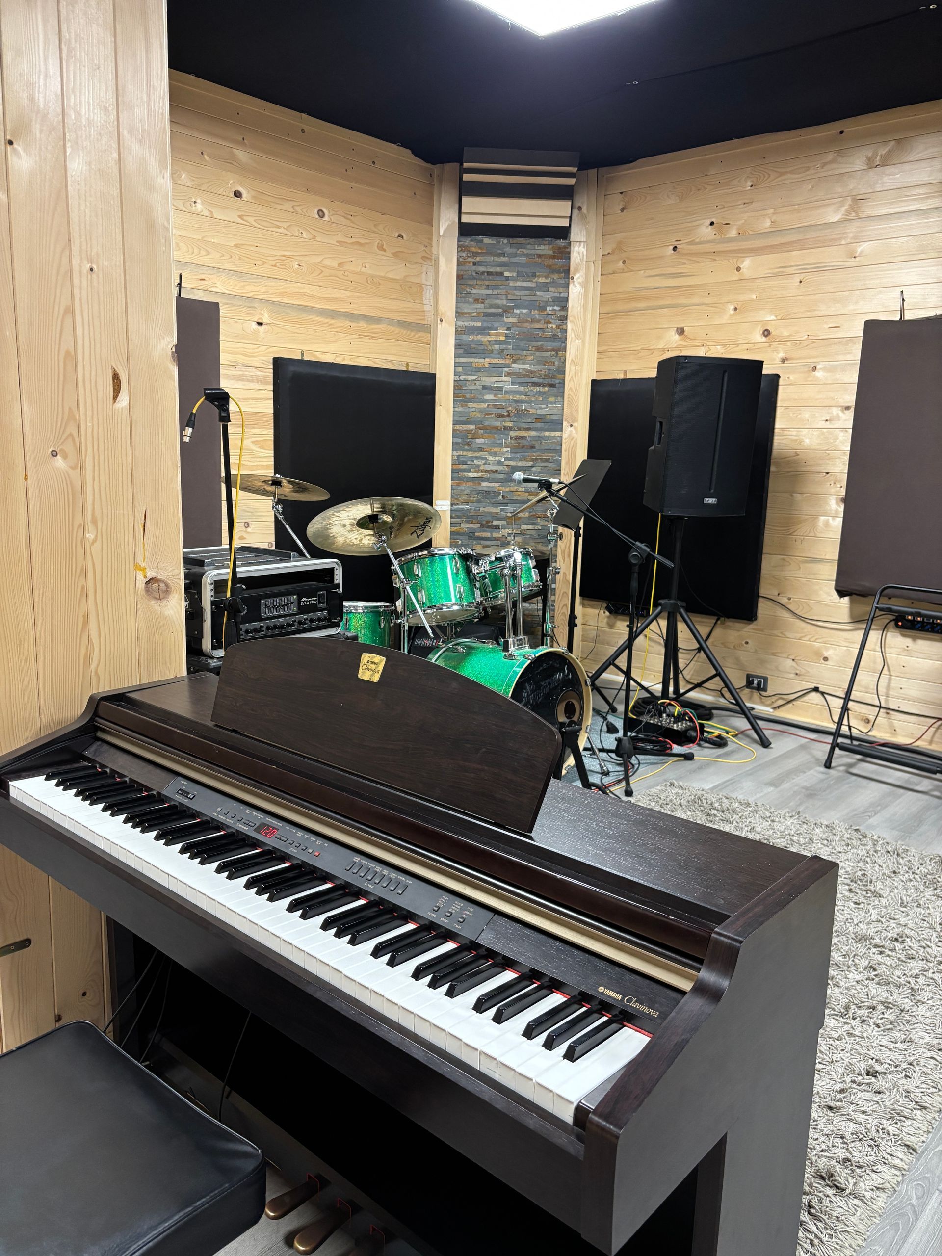 Pianoforte in uno studio musicale con batteria, altoparlanti e pannelli fonoassorbenti.