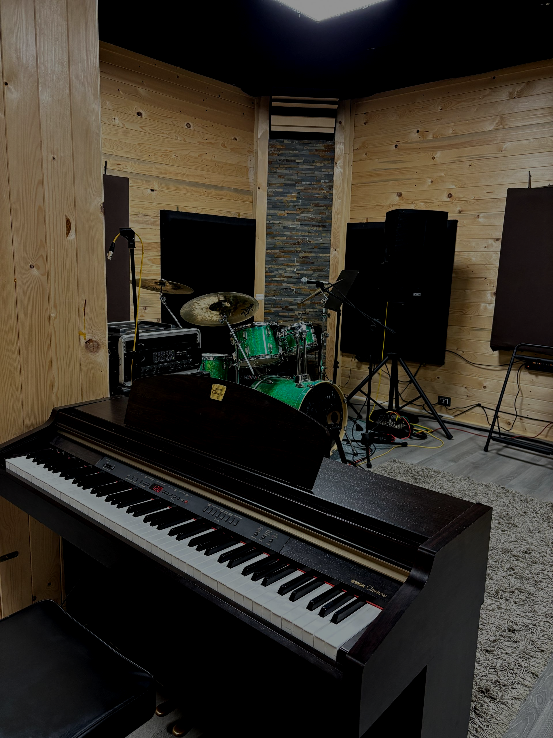 Pianoforte in uno studio di registrazione con batteria, altoparlanti e pannelli acustici. Pareti in legno.
