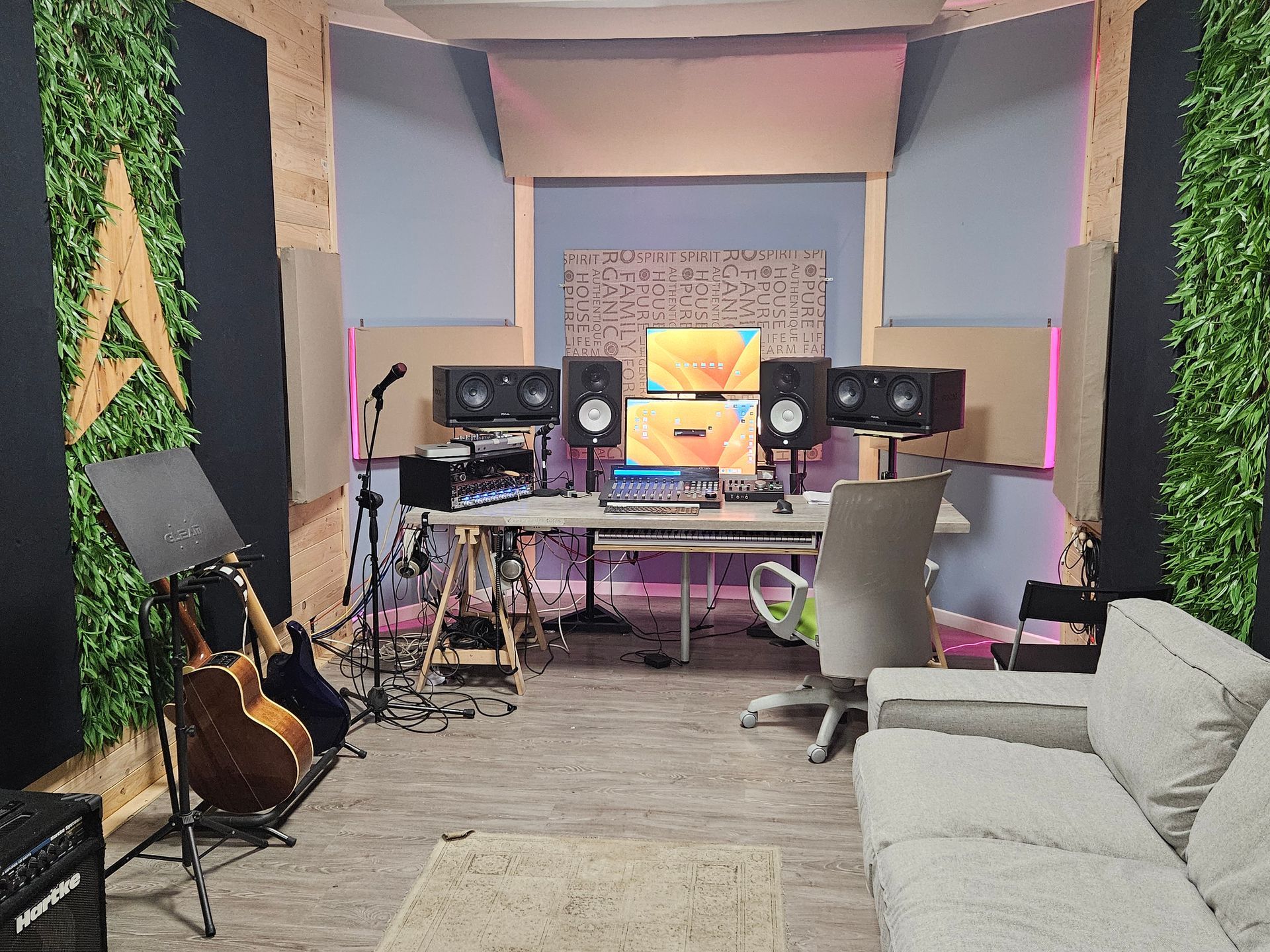 Studio di registrazione con pannelli acustici, monitor, scrivania, strumenti e divano.