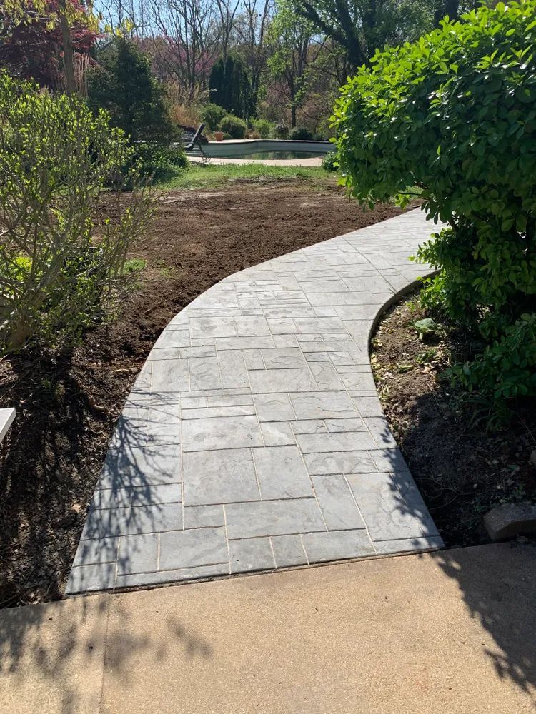 A concrete walkway going through a garden surrounded by trees and bushes.