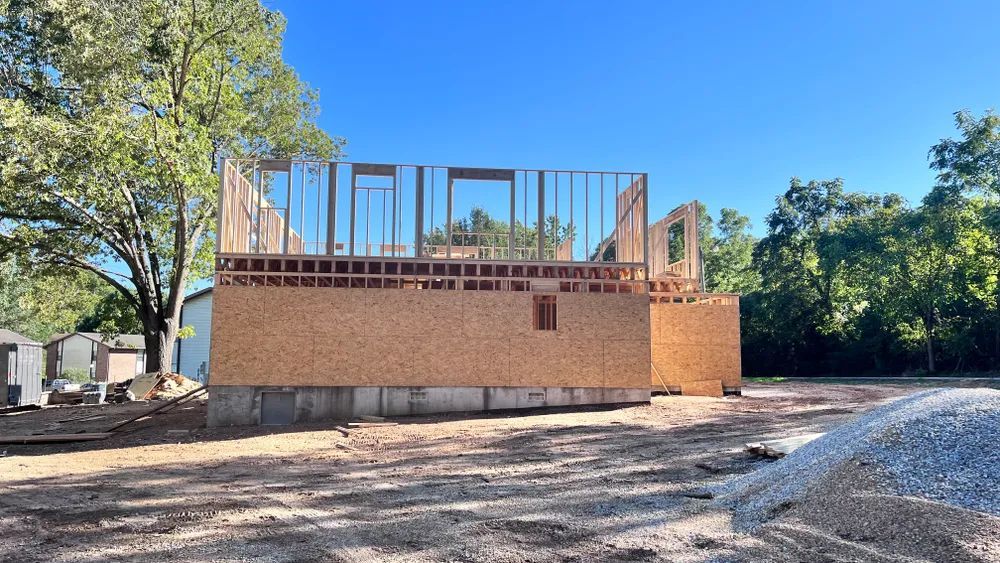A house is being built in a dirt field with trees in the background.