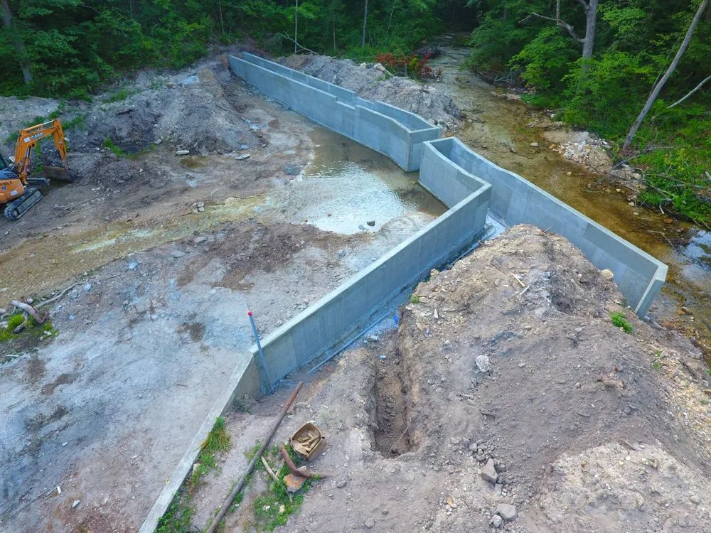 An aerial view of a concrete wall being built next to a river.