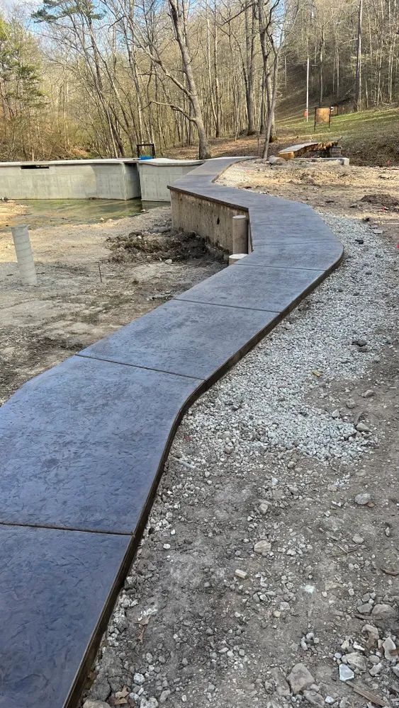 A concrete walkway going through a gravel area with trees in the background.