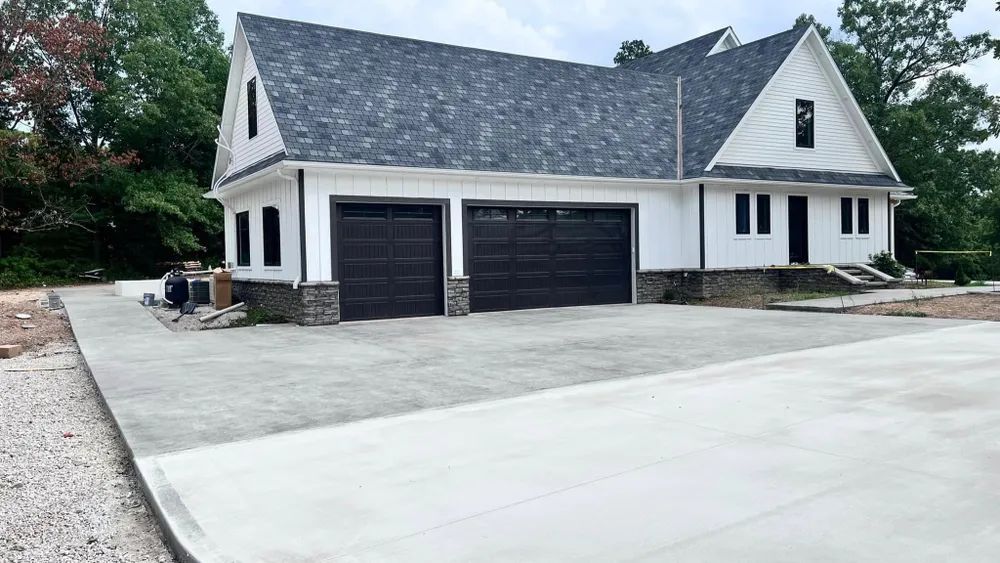 A white house with black garage doors and a concrete driveway in front of it.