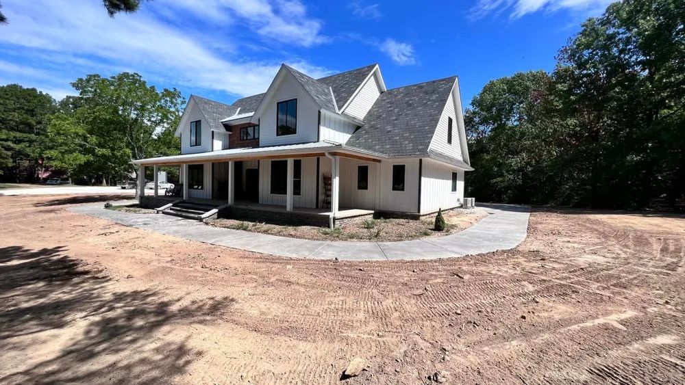 A large white house with a large porch is sitting in the middle of a dirt field.