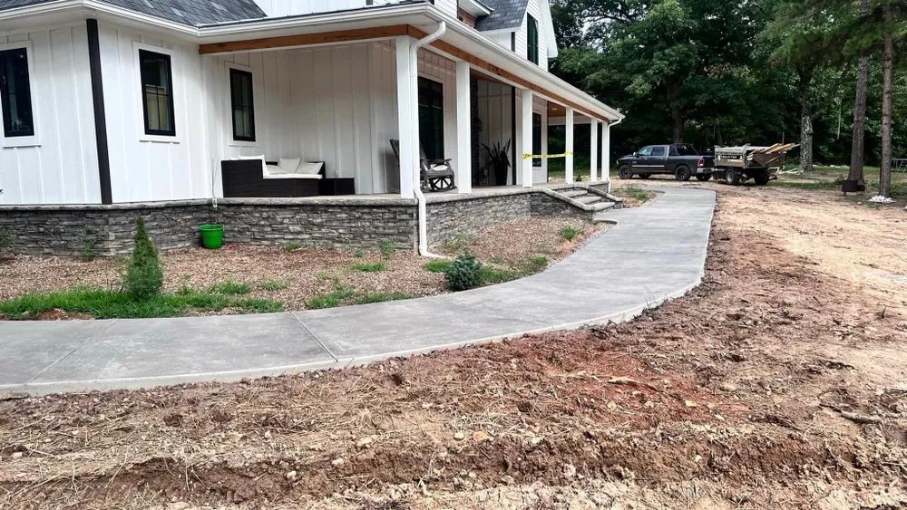 A white house with a porch and a concrete walkway leading to it.