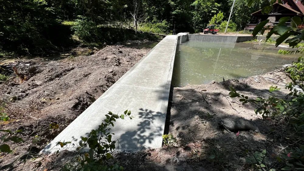 A concrete wall is surrounded by trees and a body of water.