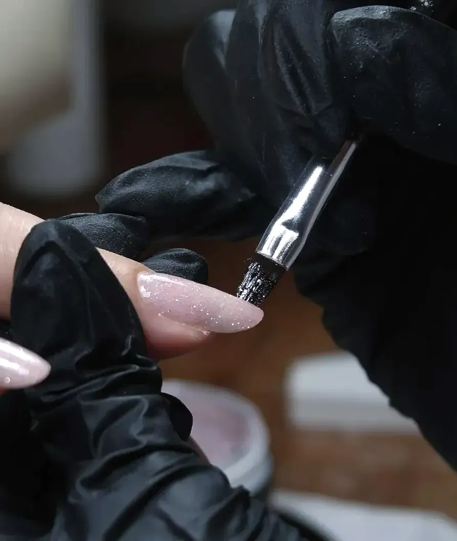 Een persoon die zwarte handschoenen draagt, brengt Builder Gel aan met een kwastje