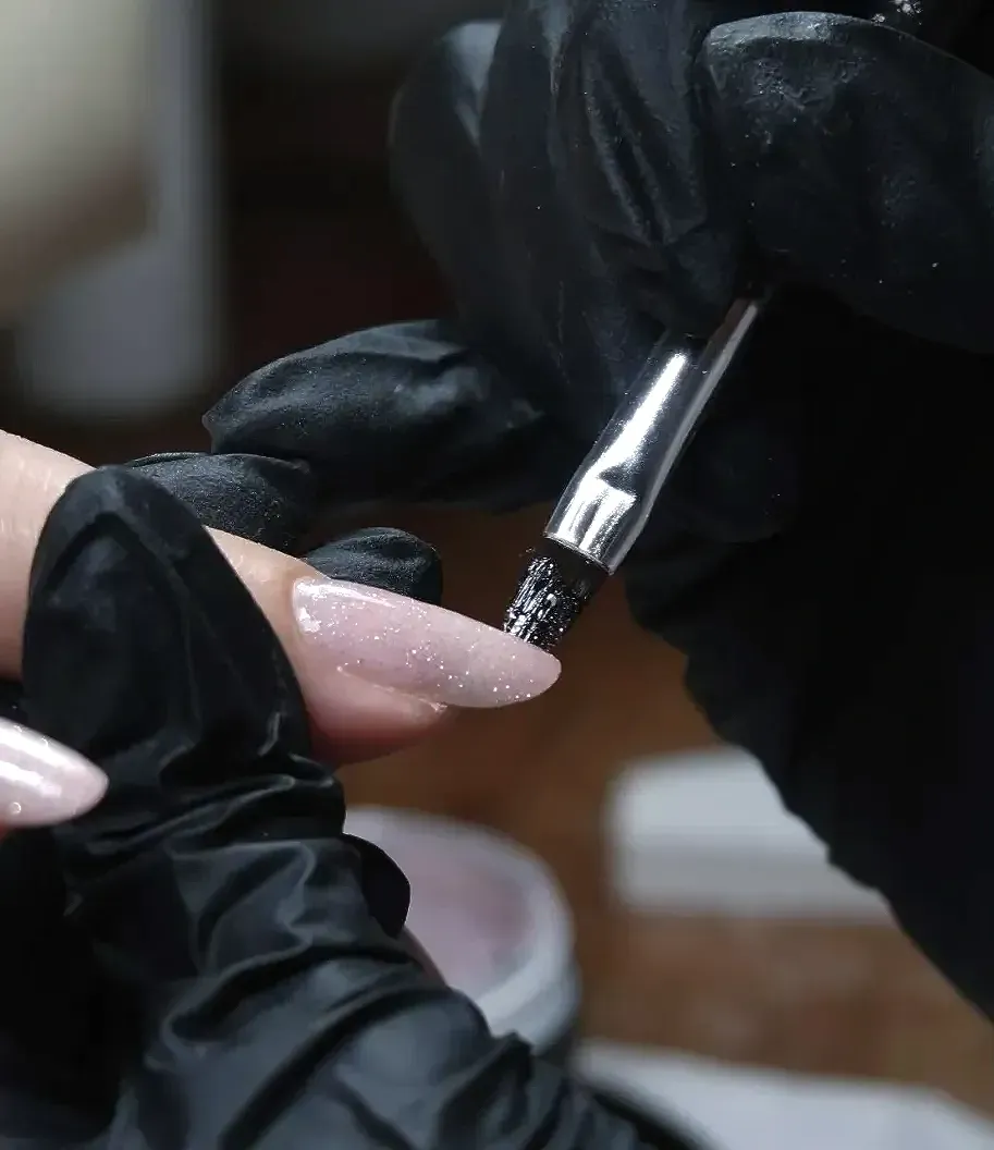 Een persoon die zwarte handschoenen draagt, brengt Builder Gel aan met een kwastje