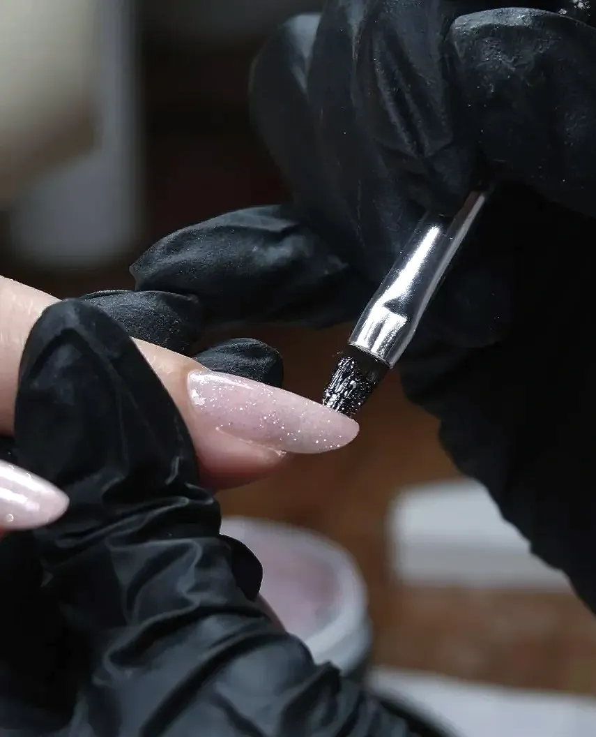 Een persoon die zwarte handschoenen draagt, brengt Builder Gel aan met een kwastje