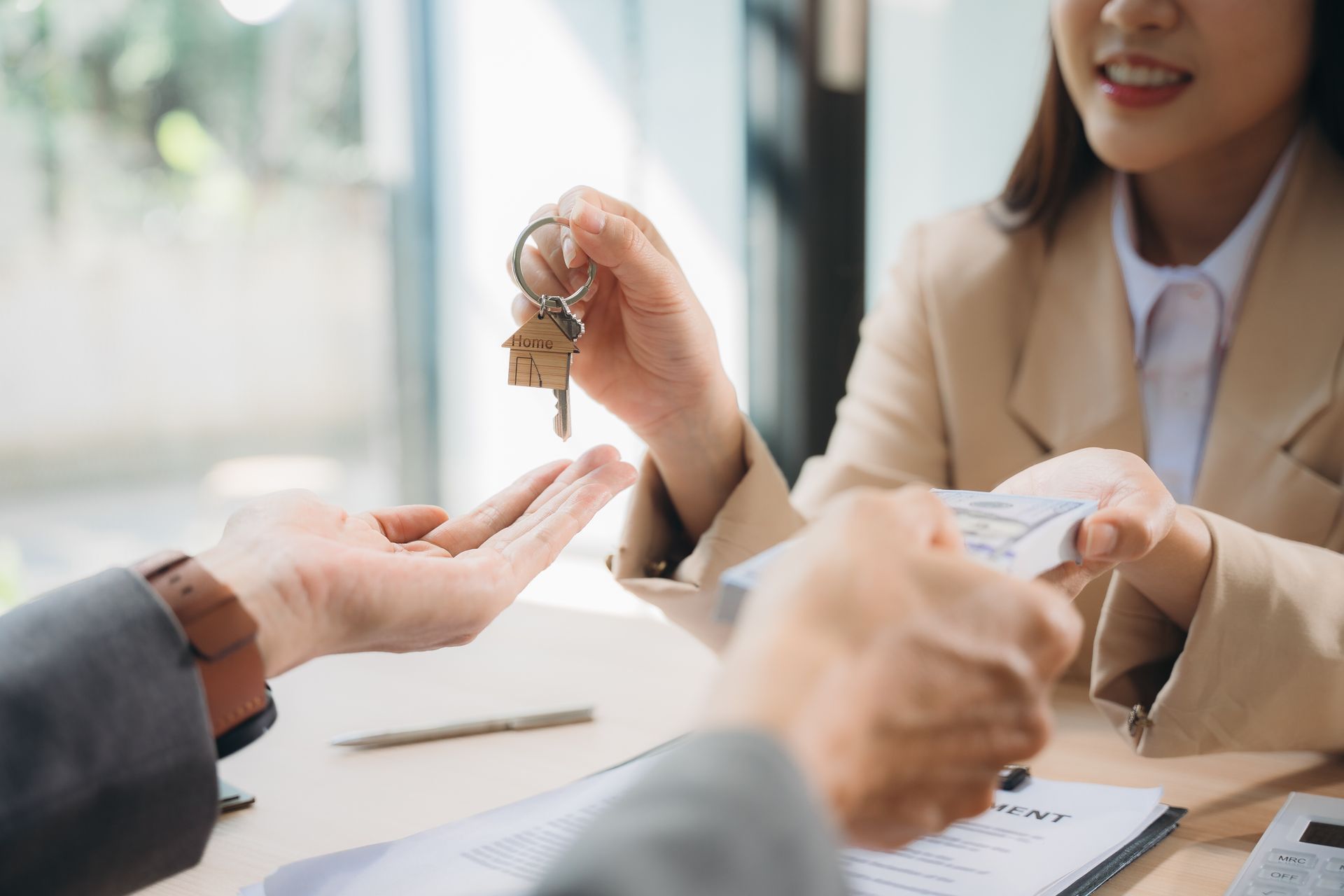 Woman handing keys with house charm to person, likely a real estate transaction.