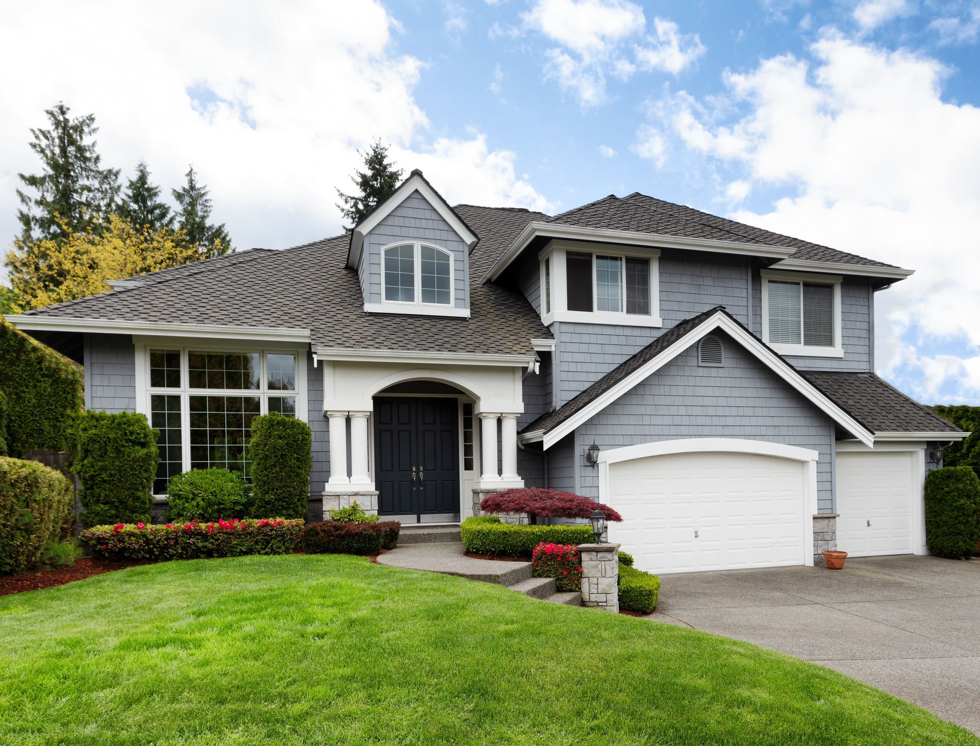 Gray house with white trim, two-car garage, manicured lawn, and blue sky.
