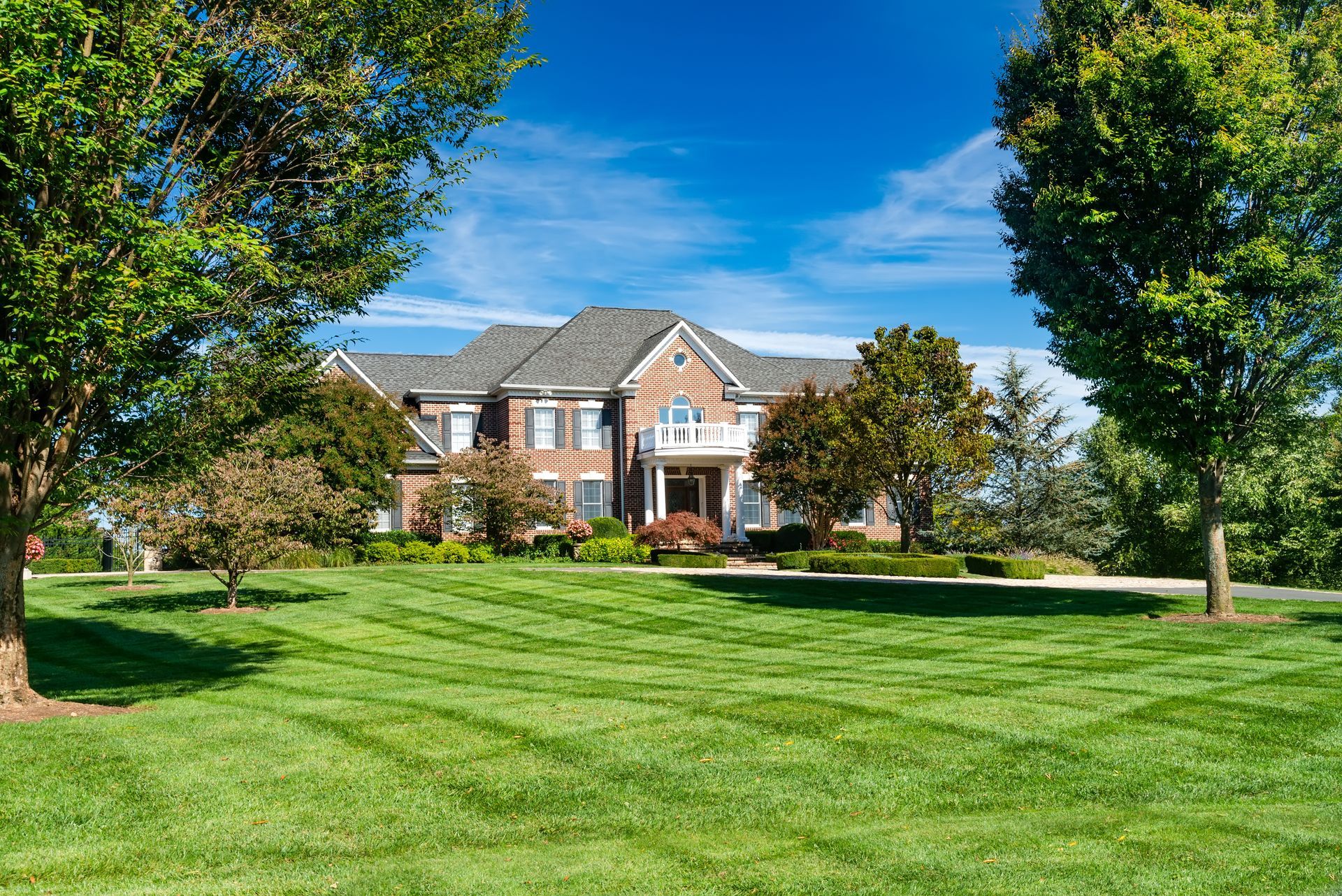 Large brick house with green lawn, blue sky, and trees.