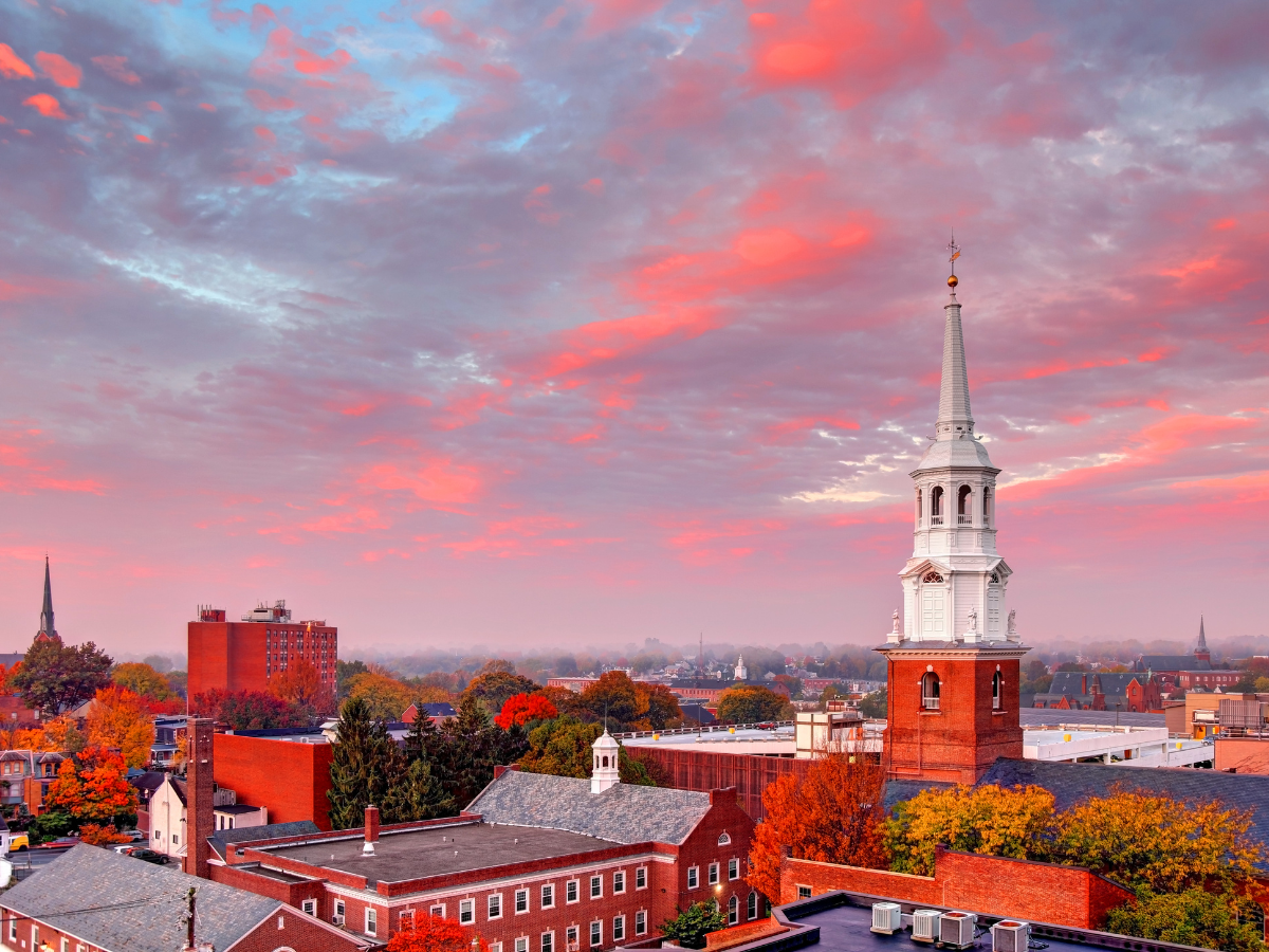 Red-brick buildings and church steeples under a vibrant pink and blue sunset in a city.