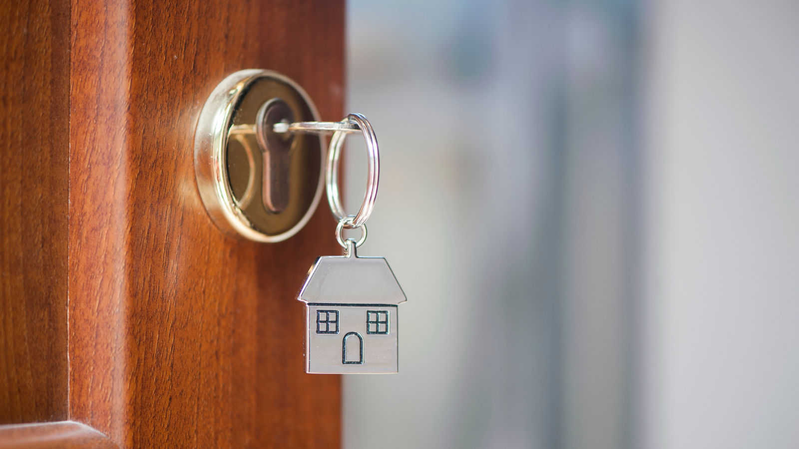 A key is hanging on a door with a house keychain.