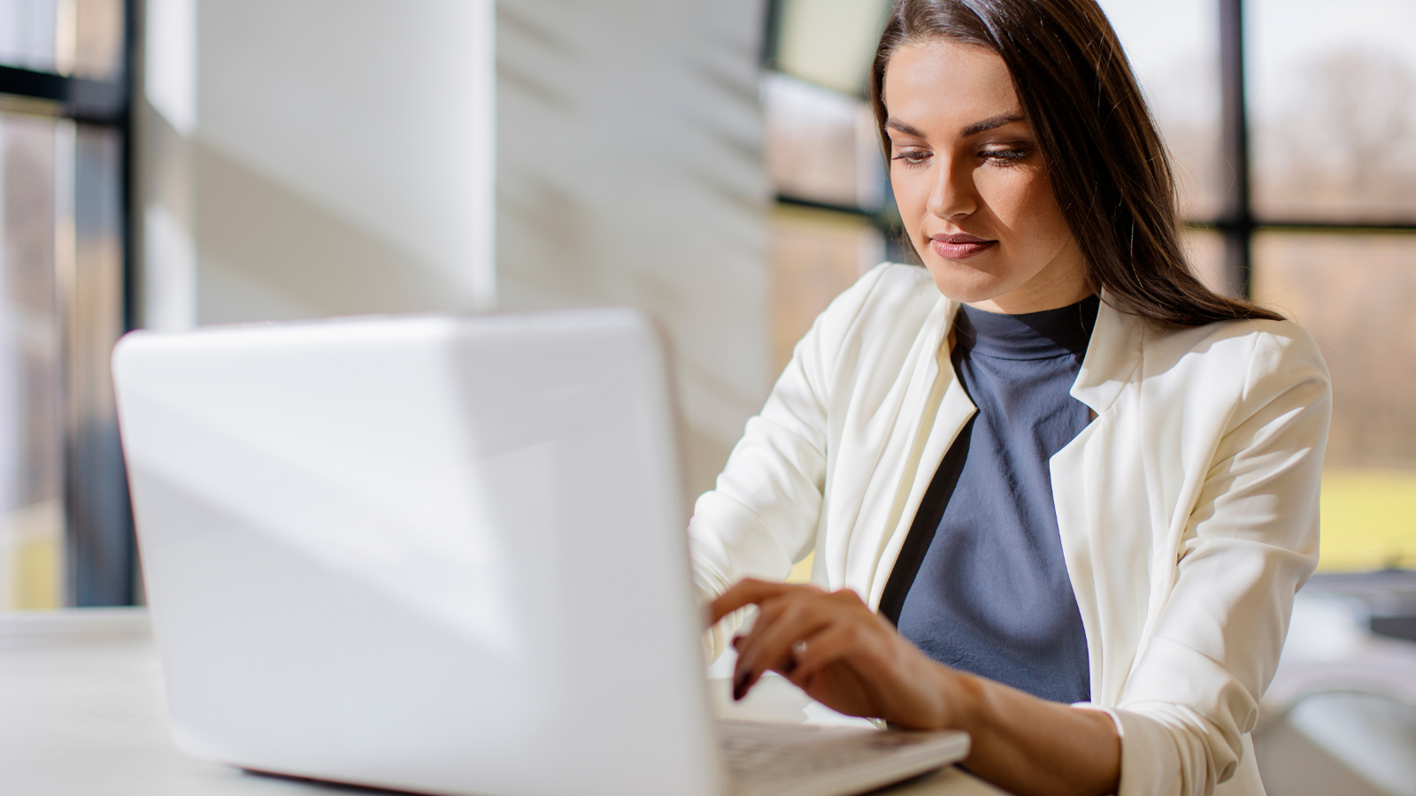 A woman is sitting at a desk using a laptop computer.