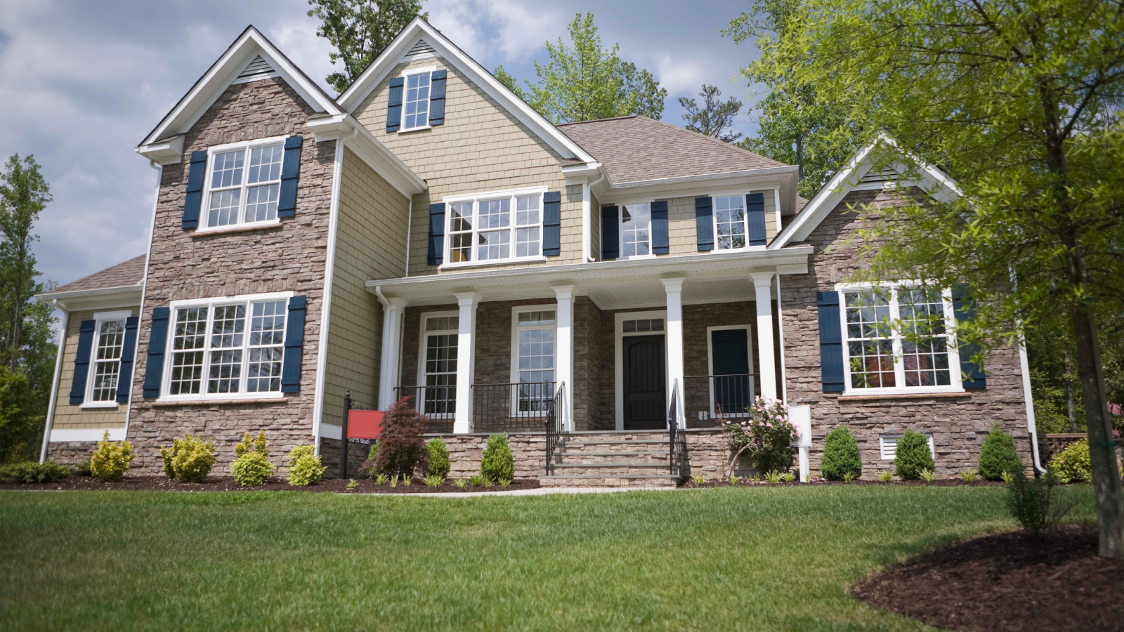 A large brick house with blue shutters is sitting on top of a lush green lawn.