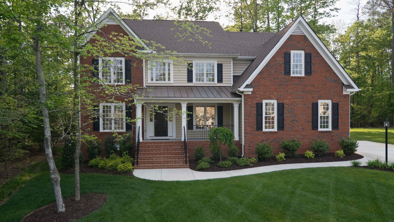 A large brick house with black shutters and a large porch