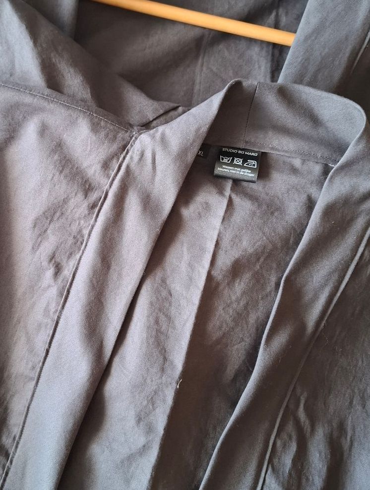Close-up van een grijze kimonotop op een houten hanger, waarbij de kraag en het label zichtbaar zijn.
