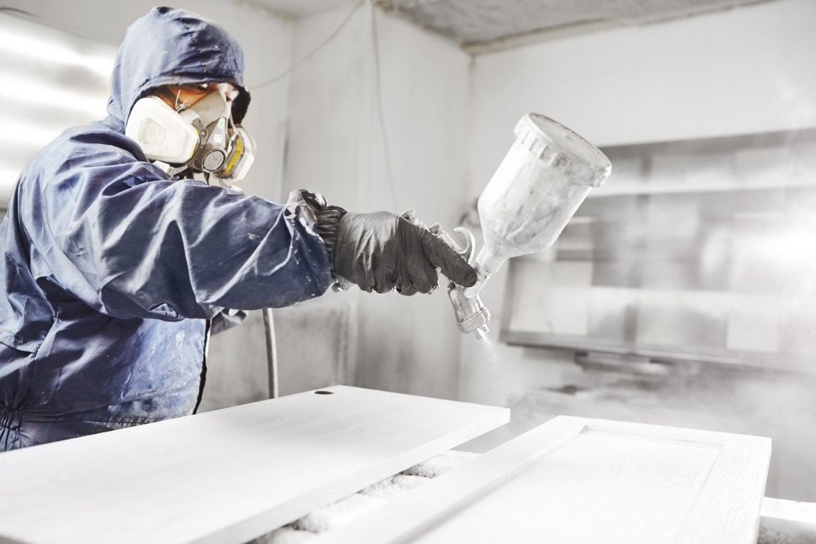 Worker in protective gear spray-painting a white surface in a paint booth