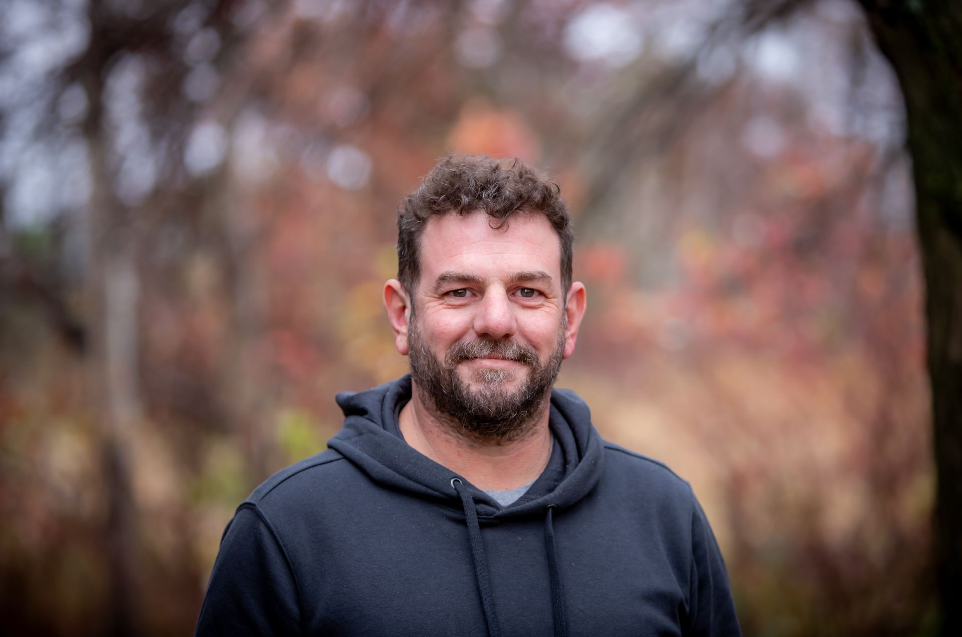 A man with a beard is wearing a black hoodie and smiling for the camera.