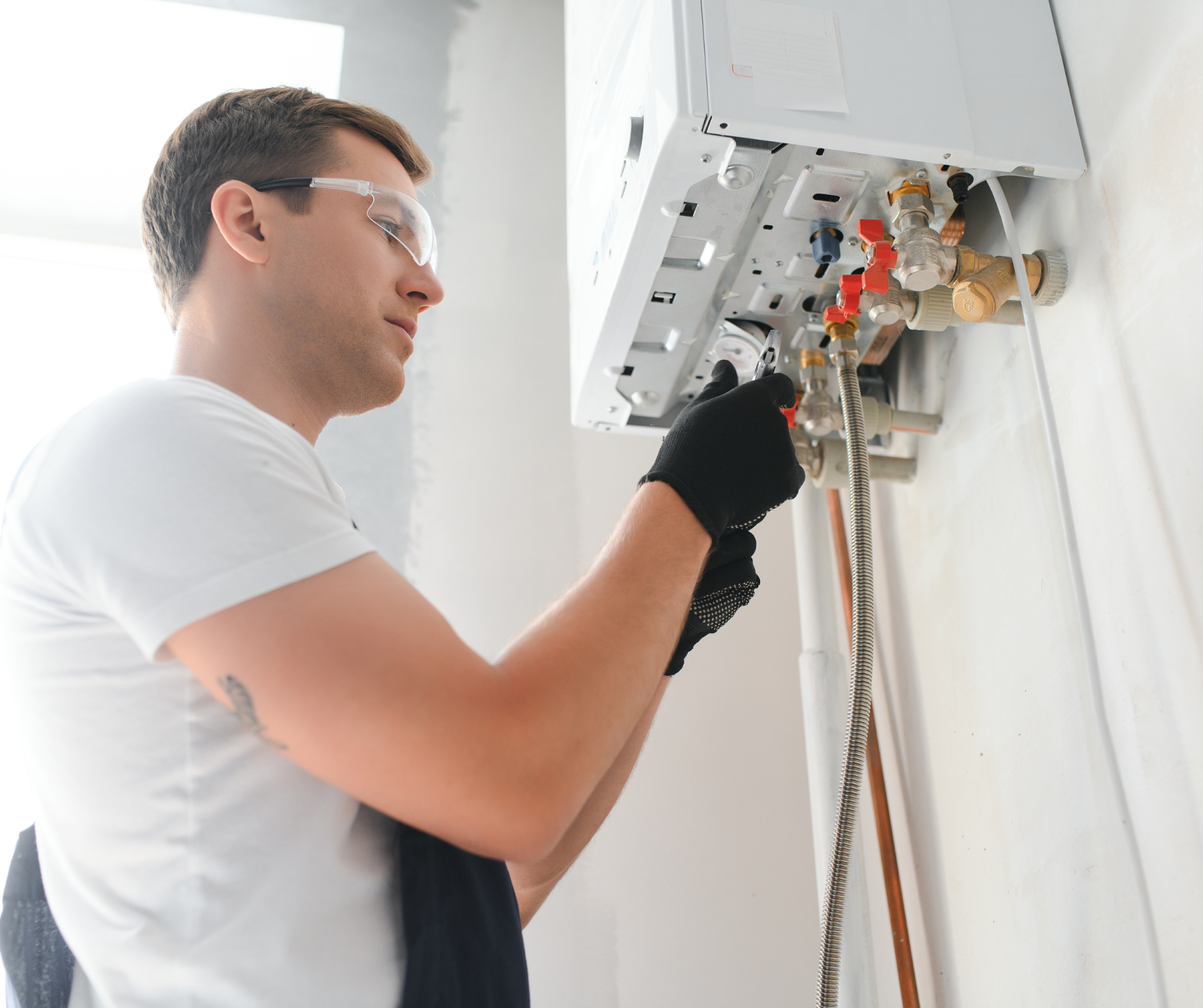 Person in safety glasses and gloves works on a white appliance on a wall.