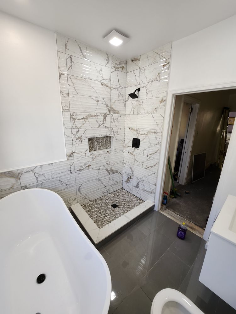 Newly renovated bathroom with marble-tiled shower, pebble floor, and a freestanding white bathtub.