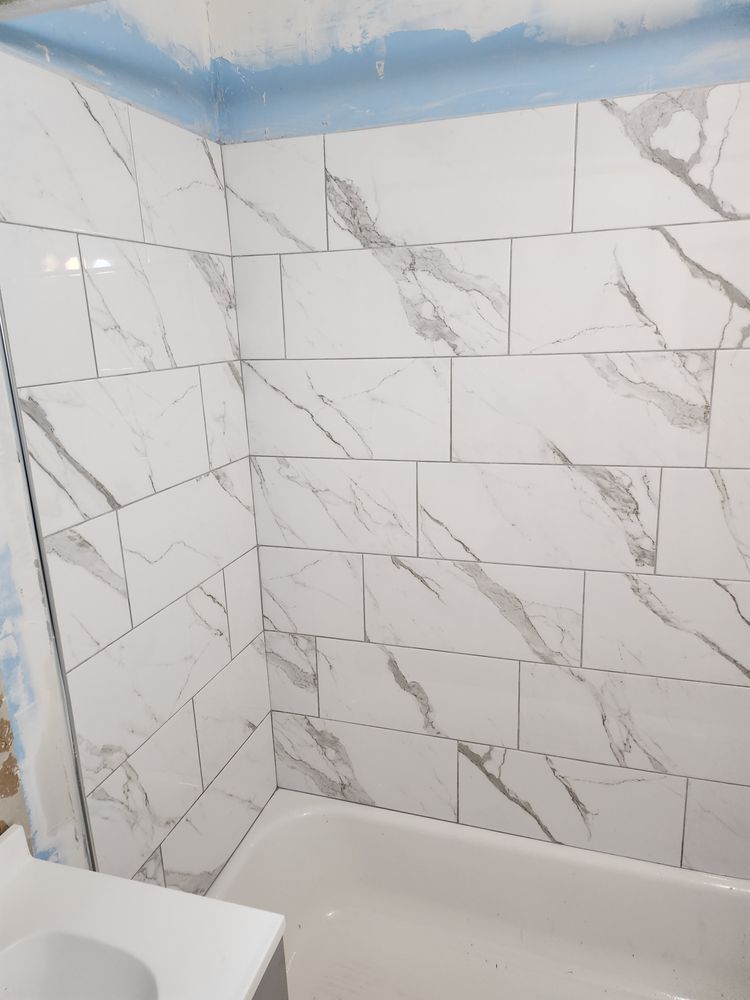 White marble-patterned tiles on a shower wall above a bathtub. Light blue paint lines the top edge.