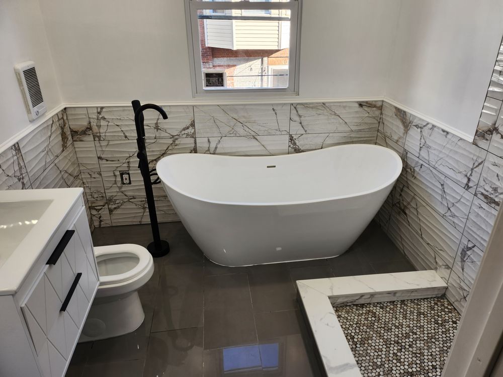 Modern bathroom with a white freestanding tub, marble-look tile, and a small shower.