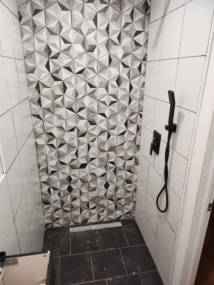 Shower stall with patterned accent wall. Dark shower floor, white tiled side walls, black shower fixtures.