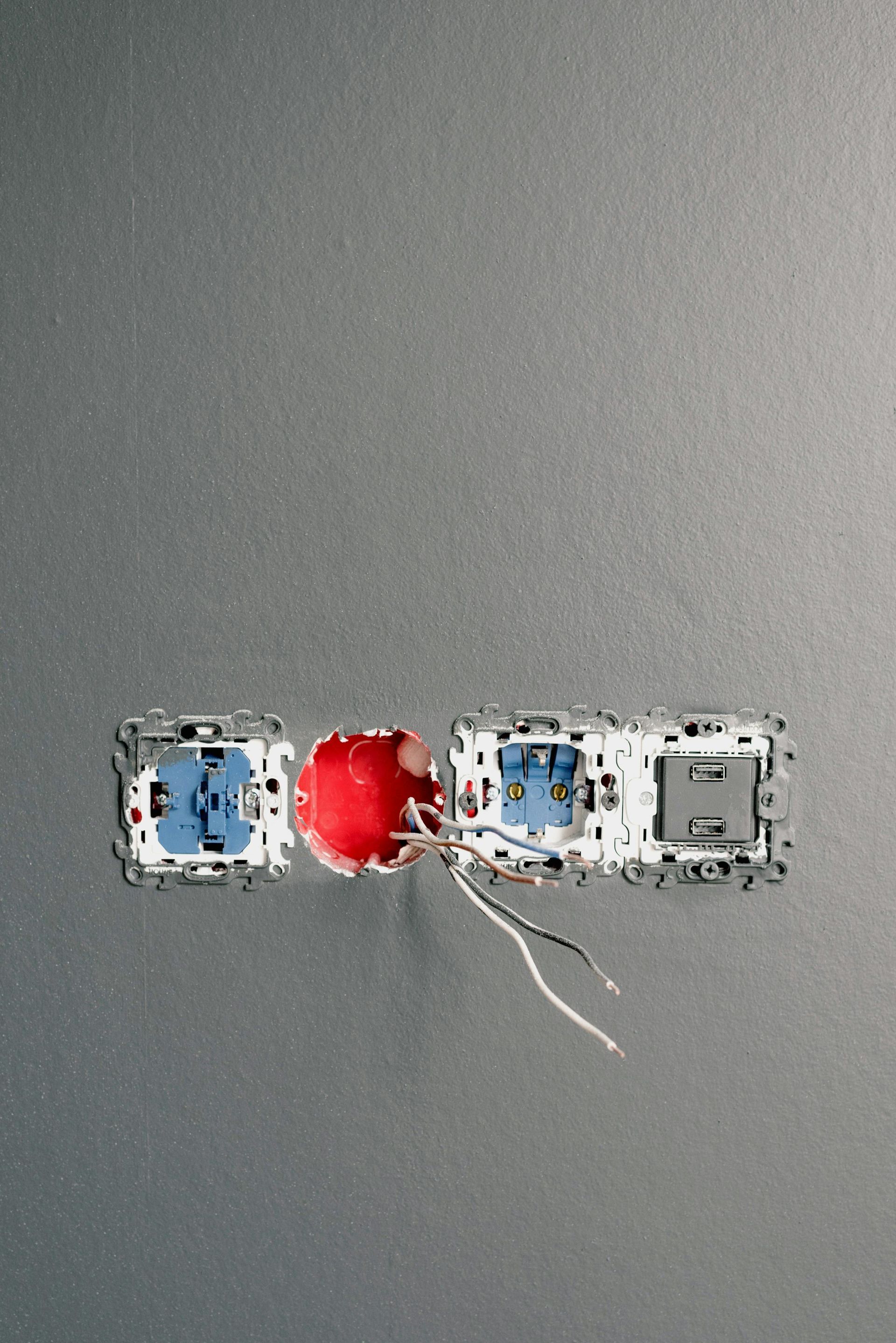 Electrical outlet box with blue and gray sockets and a red central port. White wires hang.