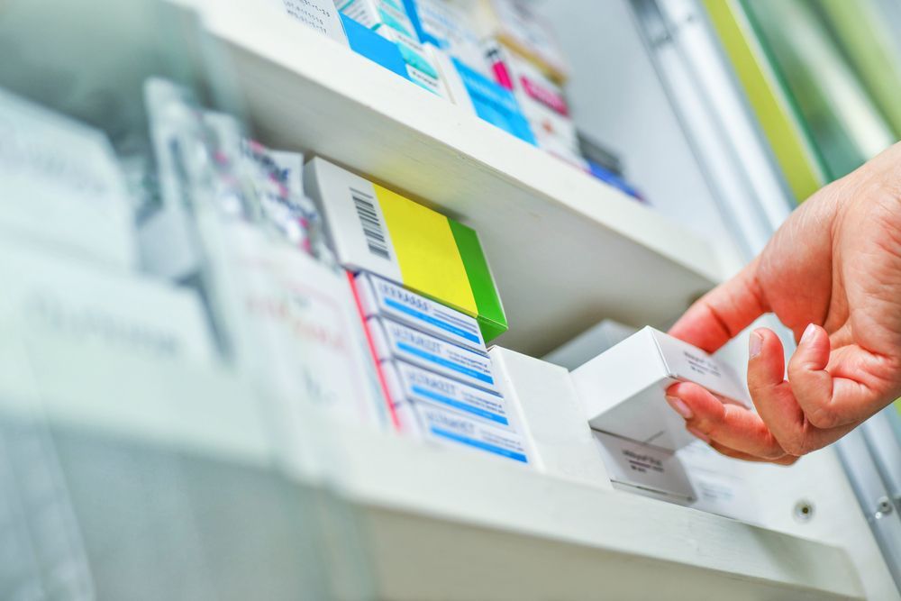 Hand Reaching for Medication Box on a Pharmacy Shelf — Blooms The Chemist Sawtell in Sawtell, NSW