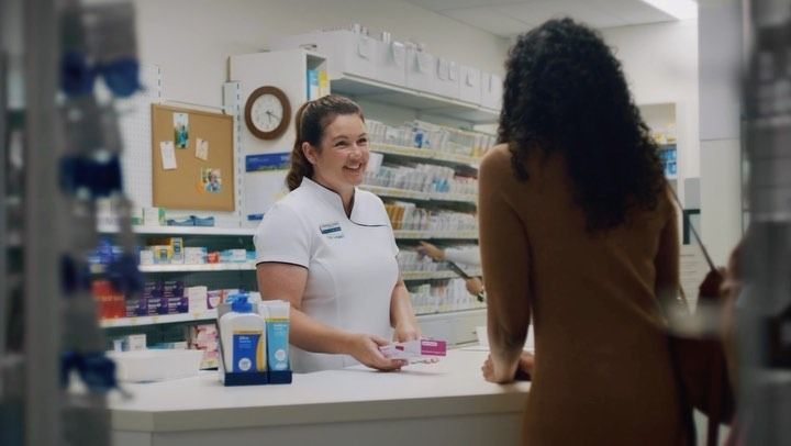 A Pharmacist Smiles, Handing a Customer a Package — Blooms The Chemist Sawtell in Sawtell, NSW