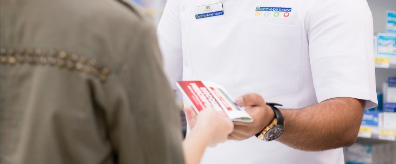 Woman Smiles, Handing a Package to a Person — Blooms The Chemist Sawtell in Sawtell, NSW