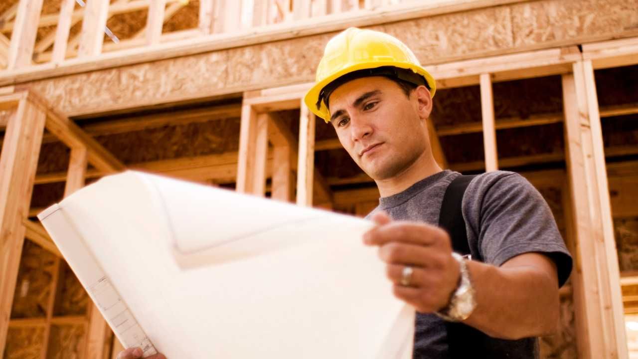 A man wearing a hard hat is holding a blueprint.