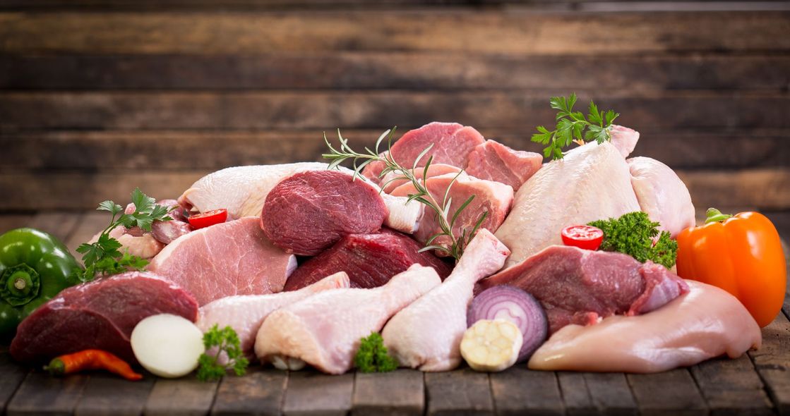Assorted raw meats and vegetables arranged on a wooden table with herbs and spices.