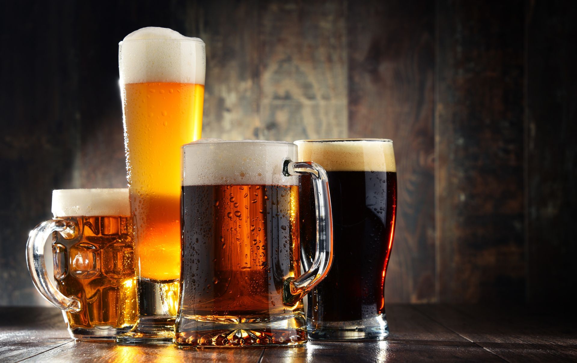 Four assorted glasses of beer on a wooden table, including a frothy tall lager and dark stout. Four assorted glasses of beer on a wooden table, including a frothy tall lager and dark stout.