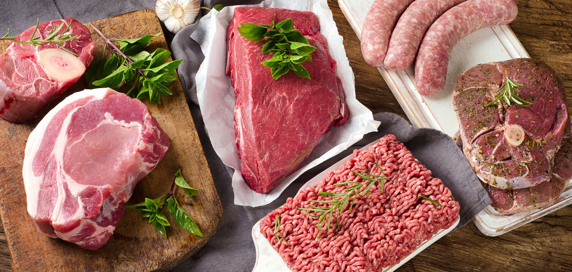 Assorted raw meats and sausages on a dark slate board, garnished with parsley.