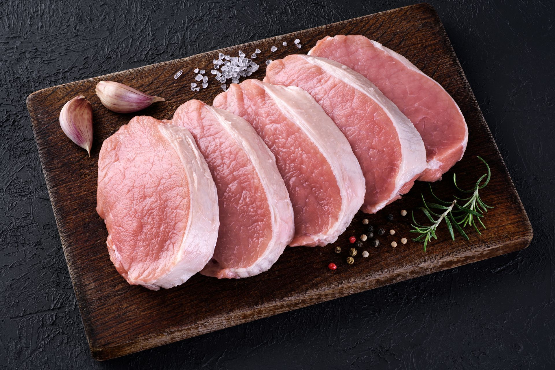 Raw pork chops arranged on a dark plate with garlic and herbs